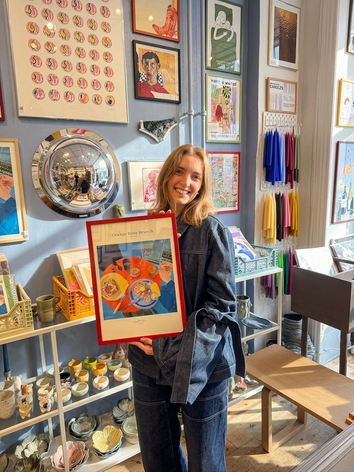Woman holding a framed artwork in a store with various items and art on the walls.